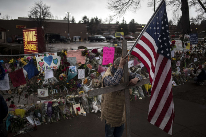 A mourner leans on a cross while holding a flag outside a memorial at a King Soopers Grocery store on March 26, 2021 in Boulder, Colorado. (Chet Strange/Getty Images/AFP)