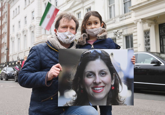 A picture of Nazanin Zaghari-Ratcliffe is shown by her husband and young daughter as they protest against her being held hostage by Iran's mullah regime. (Twitter)